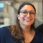A woman with long hair wearing a dark top, standing in an indoor setting.