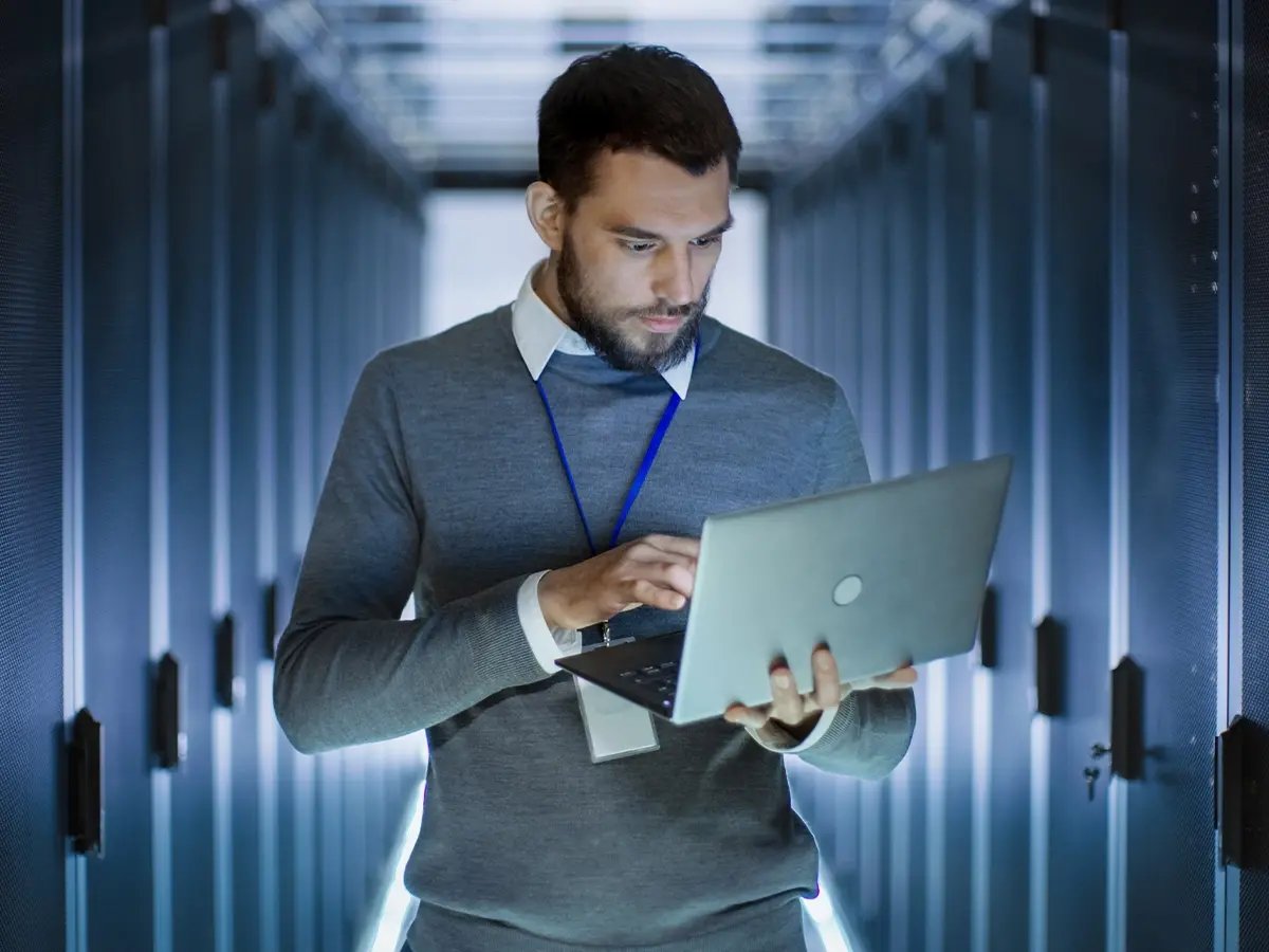 Person working on a laptop in a server room, focusing on data management and secure erasure processes.