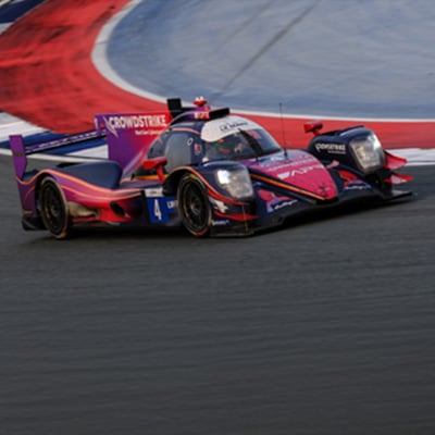 Red and black race car speeding through a track corner with blurred background showing motion