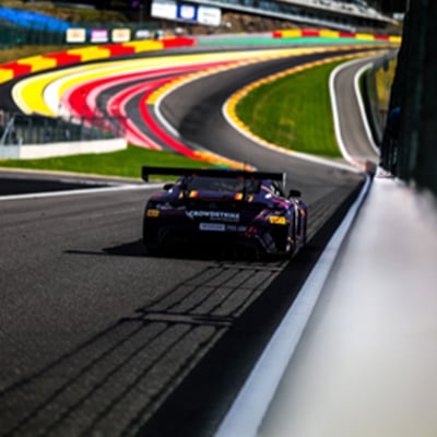 Race car driving along a curved track with vibrant red, yellow, and green painted sections