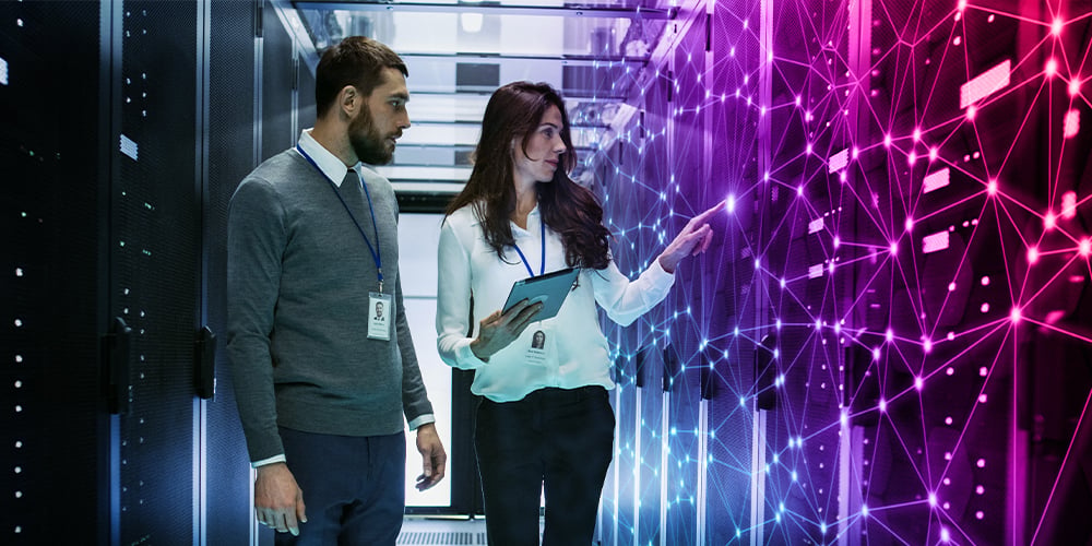 Two people in a server room reviewing a tablet, with a glowing digital network overlay on the right