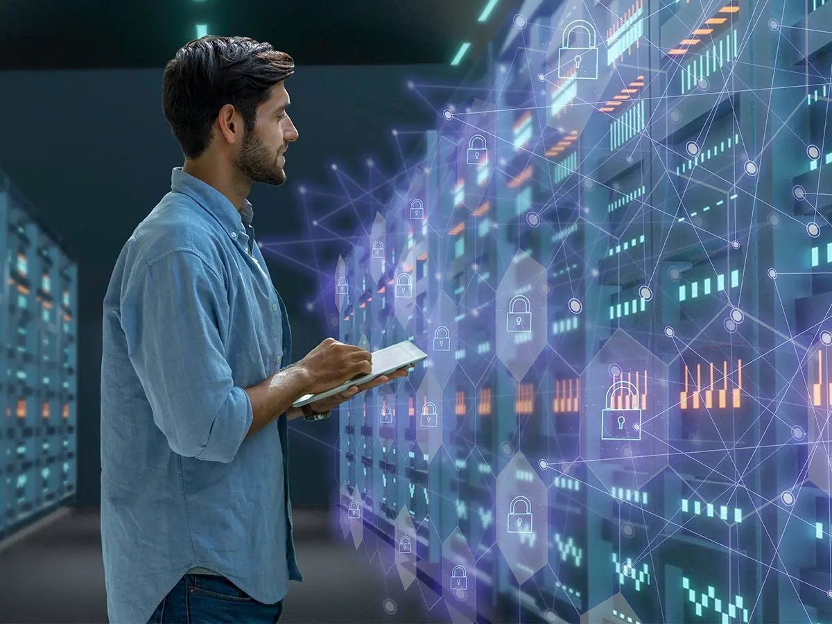 Person holding a tablet while standing in a server room with illuminated racks and digital security icons overlayed, representing enterprise storage and data protection.