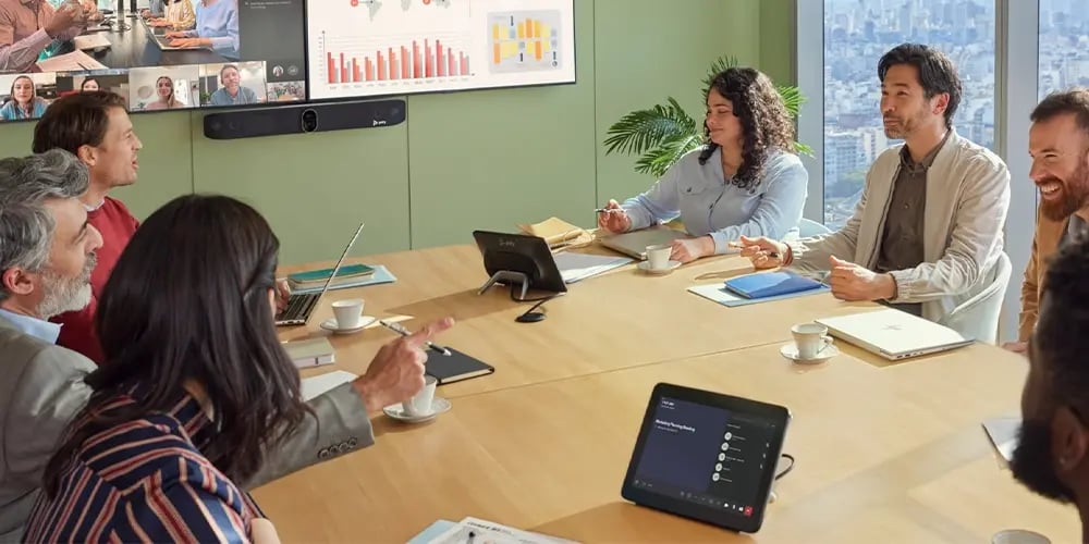 Team in a meeting room with a large screen displaying charts and video call participants.
