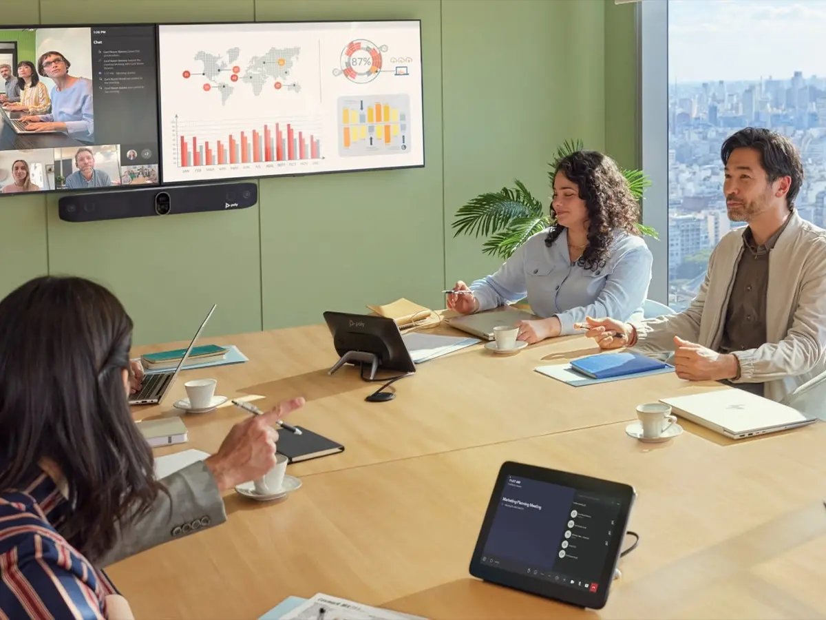 Team in a meeting room with a large screen displaying charts and video call participants.