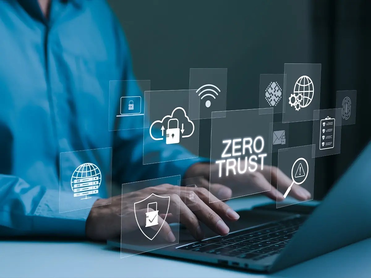 Hands typing on a laptop with floating digital security icons and the words ‘Zero Trust.’