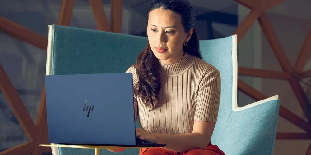 Person using an HP laptop while seated on a modern chair, representing an AI-powered notebook for productivity.