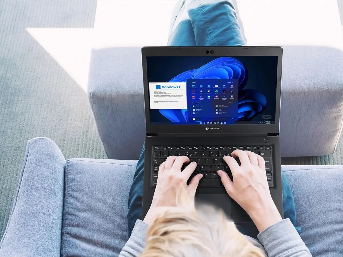 Laptop displaying the Windows 11 home screen and setup window, placed on a person's lap while typing.