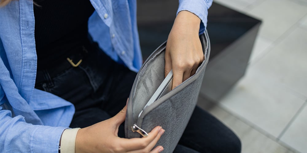 Person sliding a laptop into a grey fabric sleeve while seated.