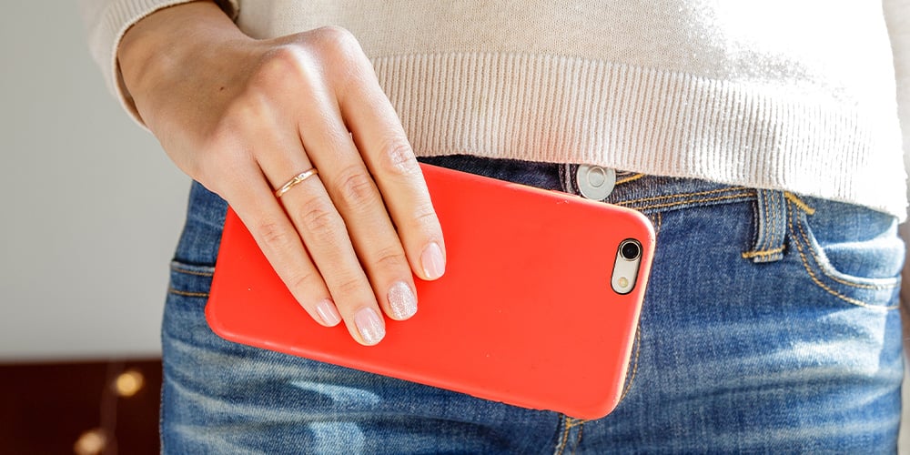 Hand holding a smartphone against a person’s jeans pocket.