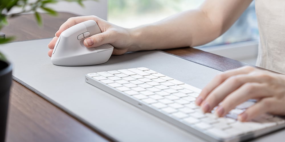 Person using an ergonomic mouse and keyboard on a desk.