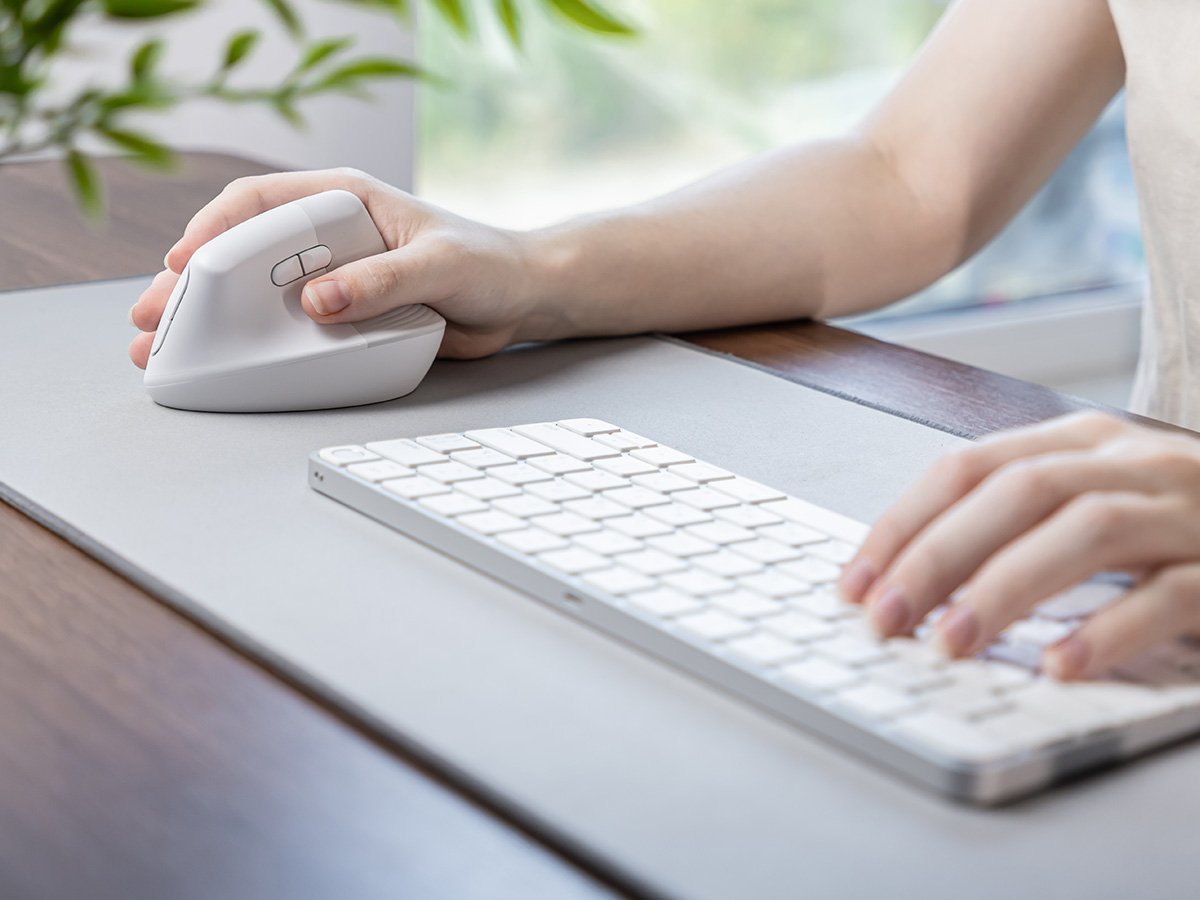 Person using an ergonomic mouse and keyboard on a desk.