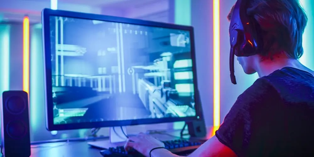 A person wearing a headset plays a video game on a computer, surrounded by neon lights. The atmosphere is immersive and focused, with vibrant colors.
