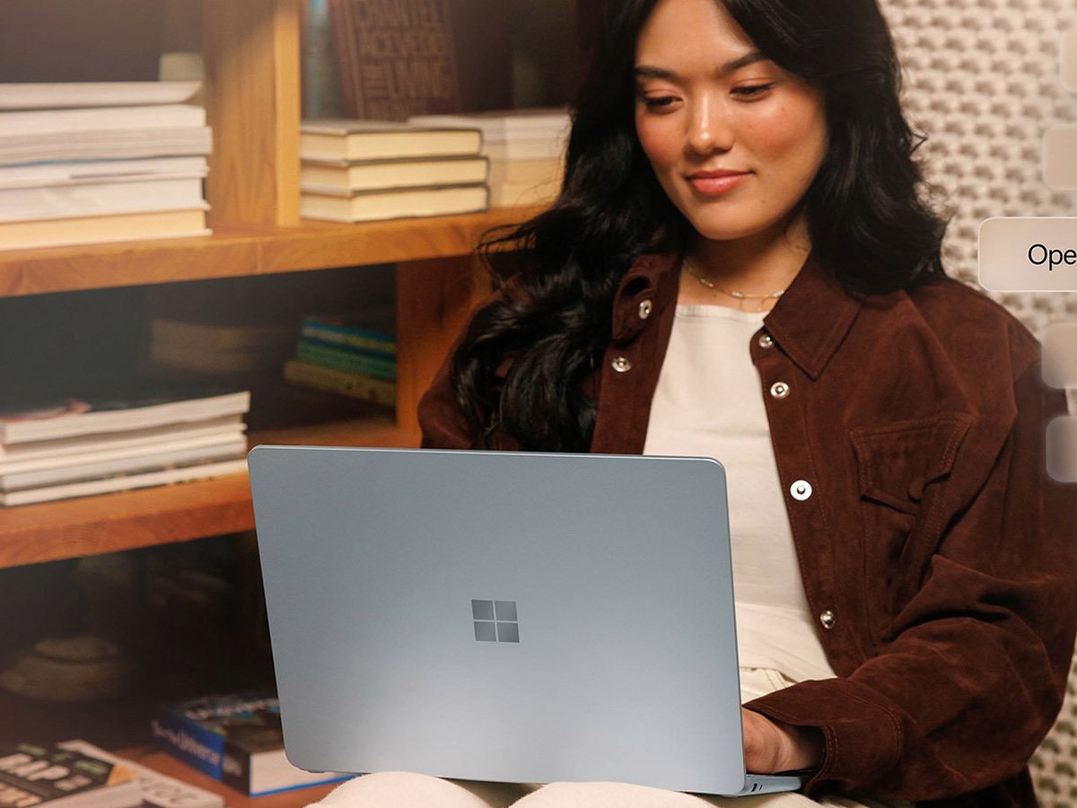 Person using a silver laptop while seated near a bookshelf.