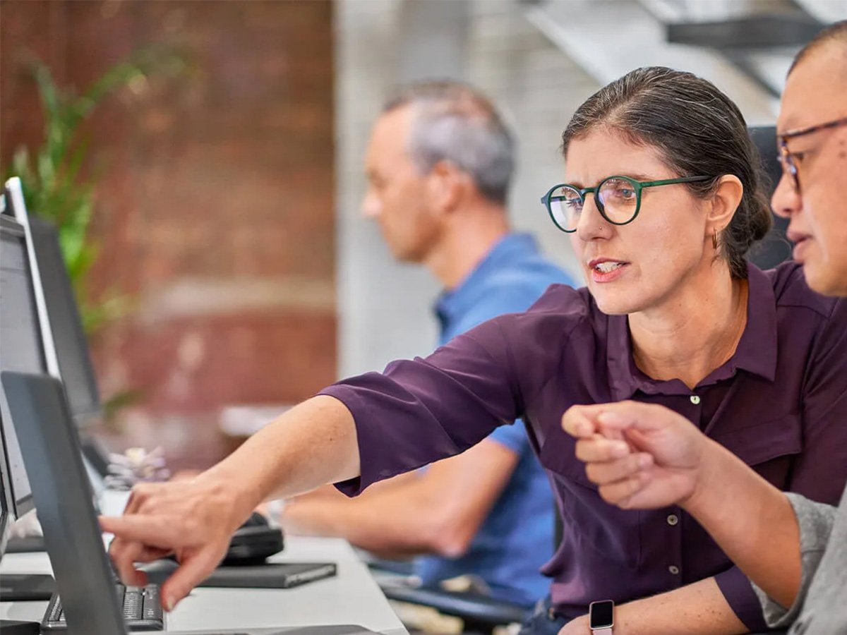 Person pointing at a computer screen during a discussion in an office setting.