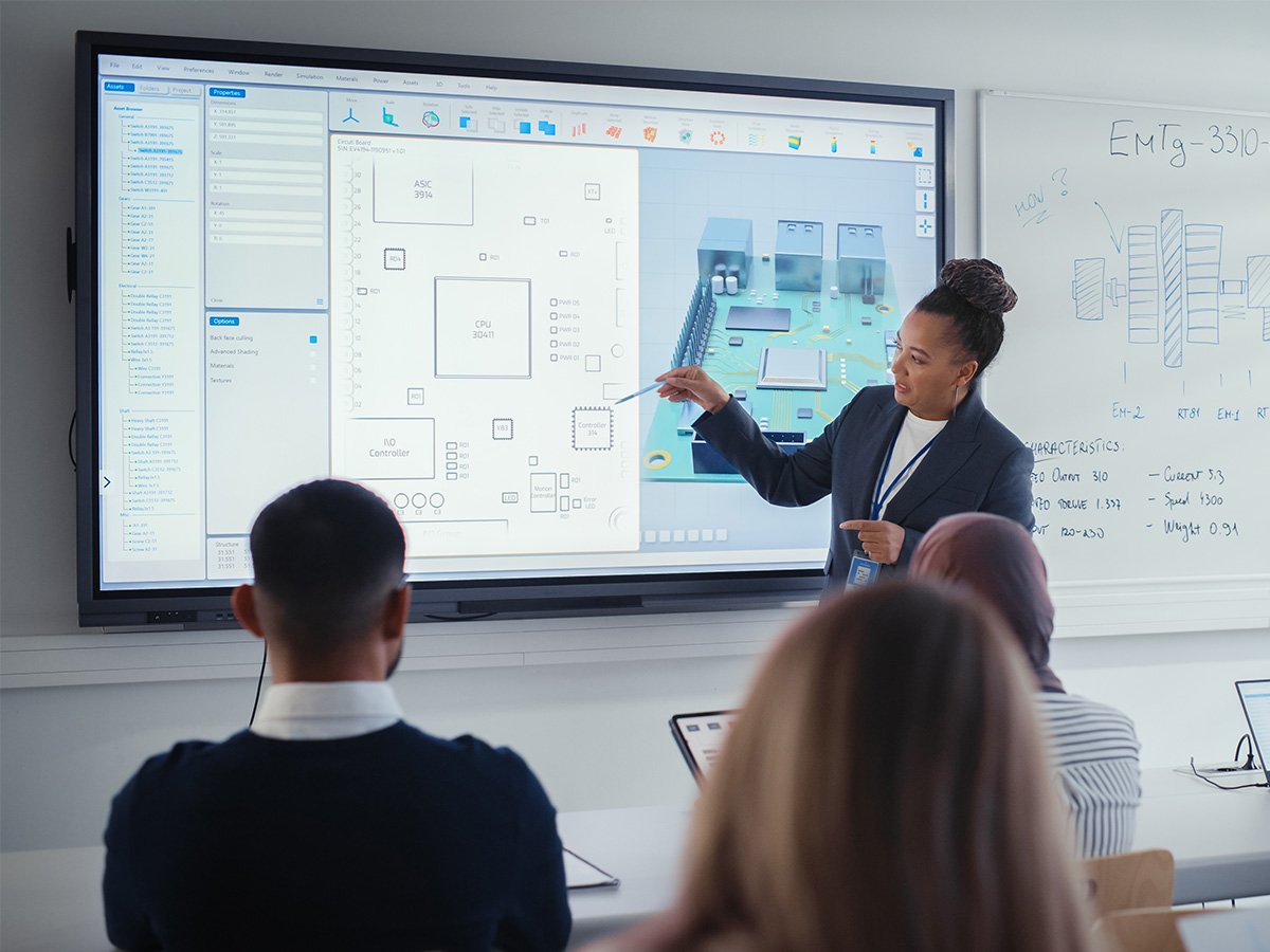 Presenter explaining a technical diagram on a large interactive display to a seated audience.
