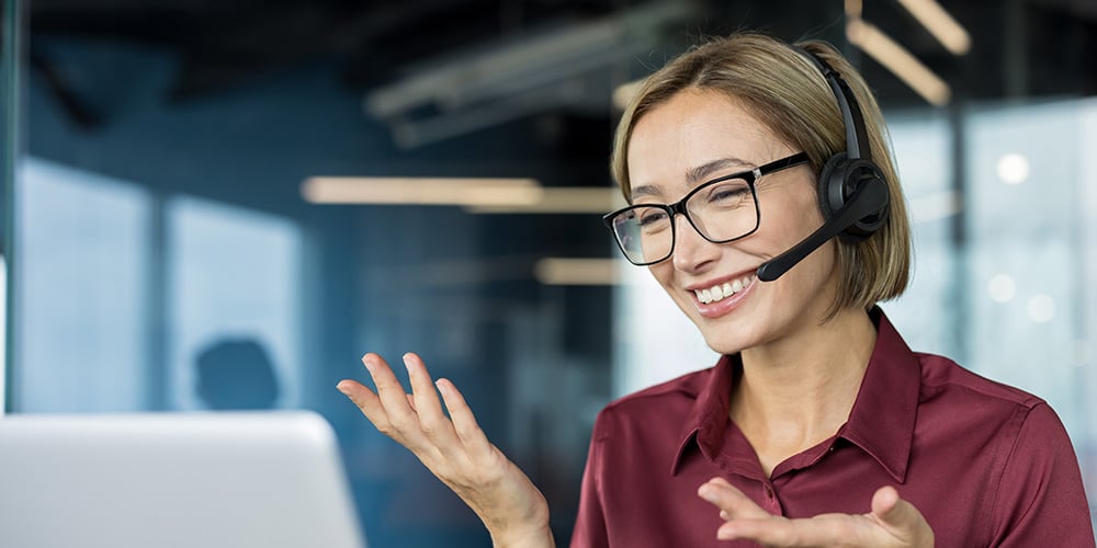 Person wearing a headset speaking and gesturing during a video call at a desk.
