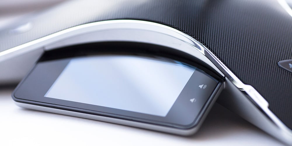 Close-up of a modern conference speakerphone with a touchscreen control panel.