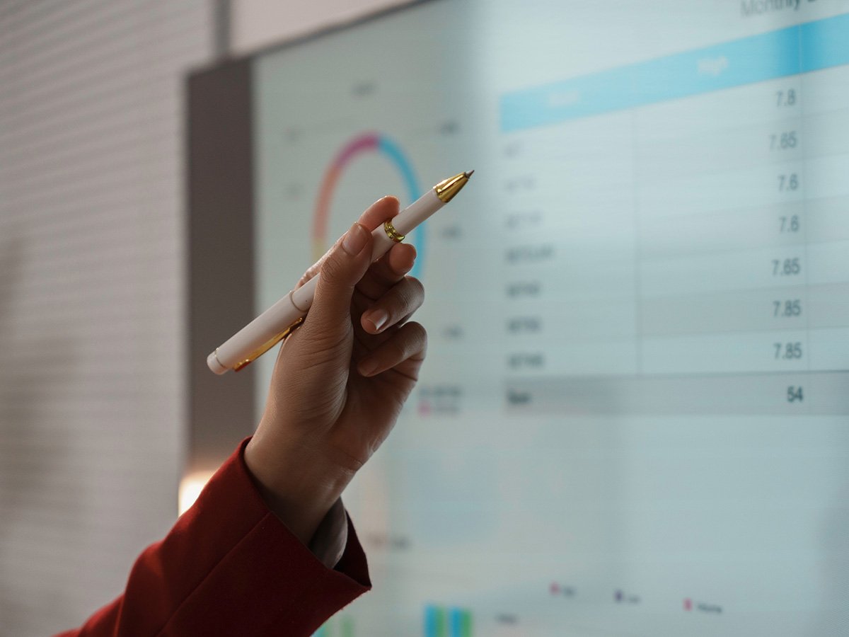 Person pointing at a large display showing charts and data in a presentation setting.
