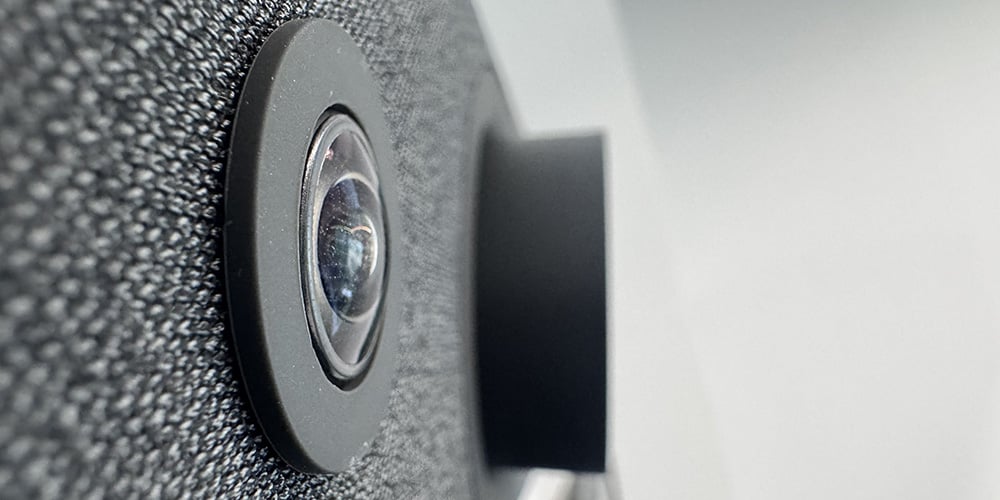Close-up of a wide‑angle video conferencing camera lens on a textured device.