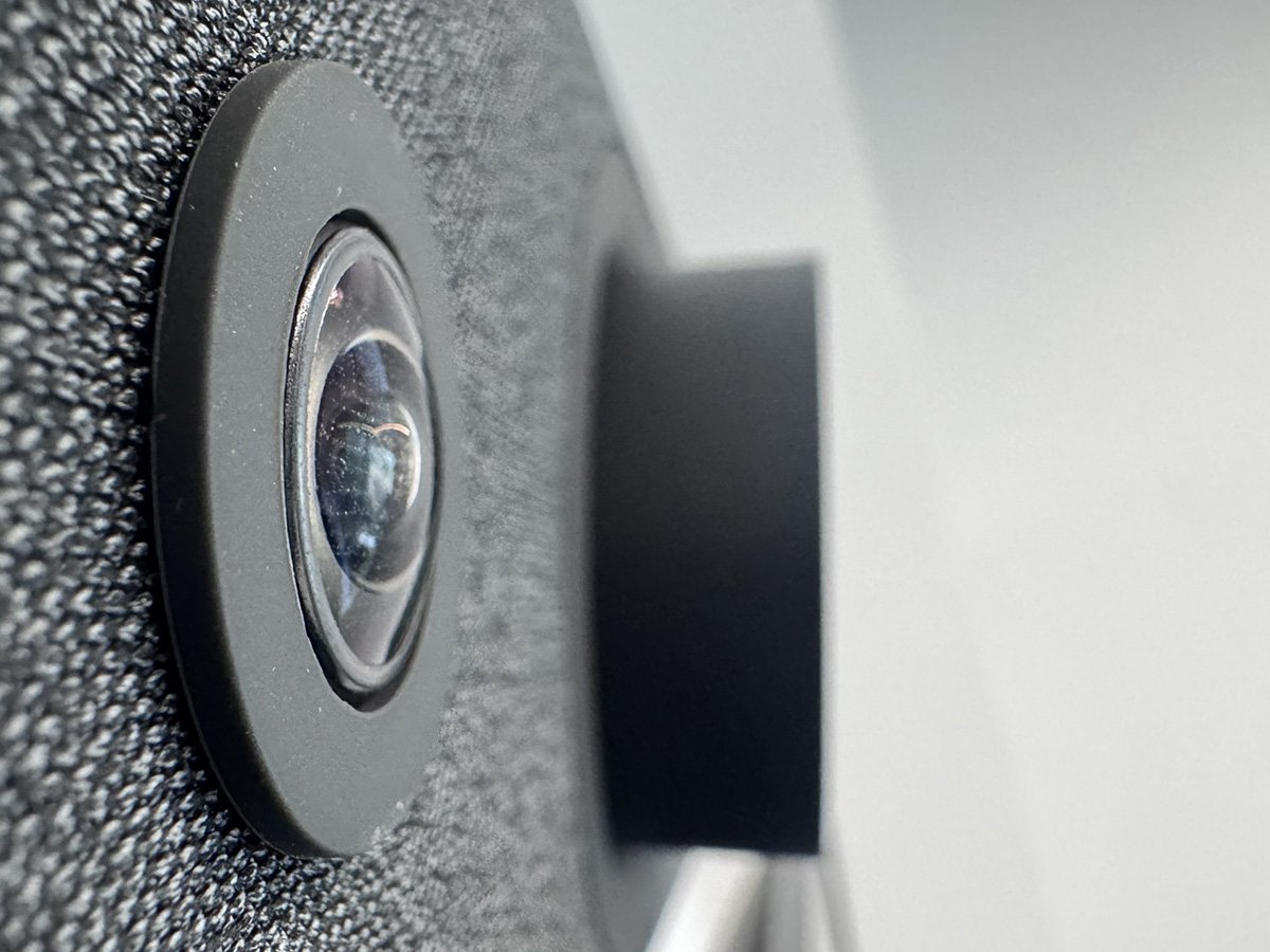 Close-up of a wide‑angle video conferencing camera lens on a textured device.
