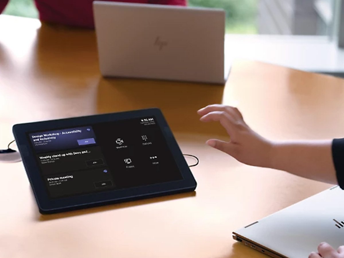 Person using a touchscreen meeting control panel on a table.