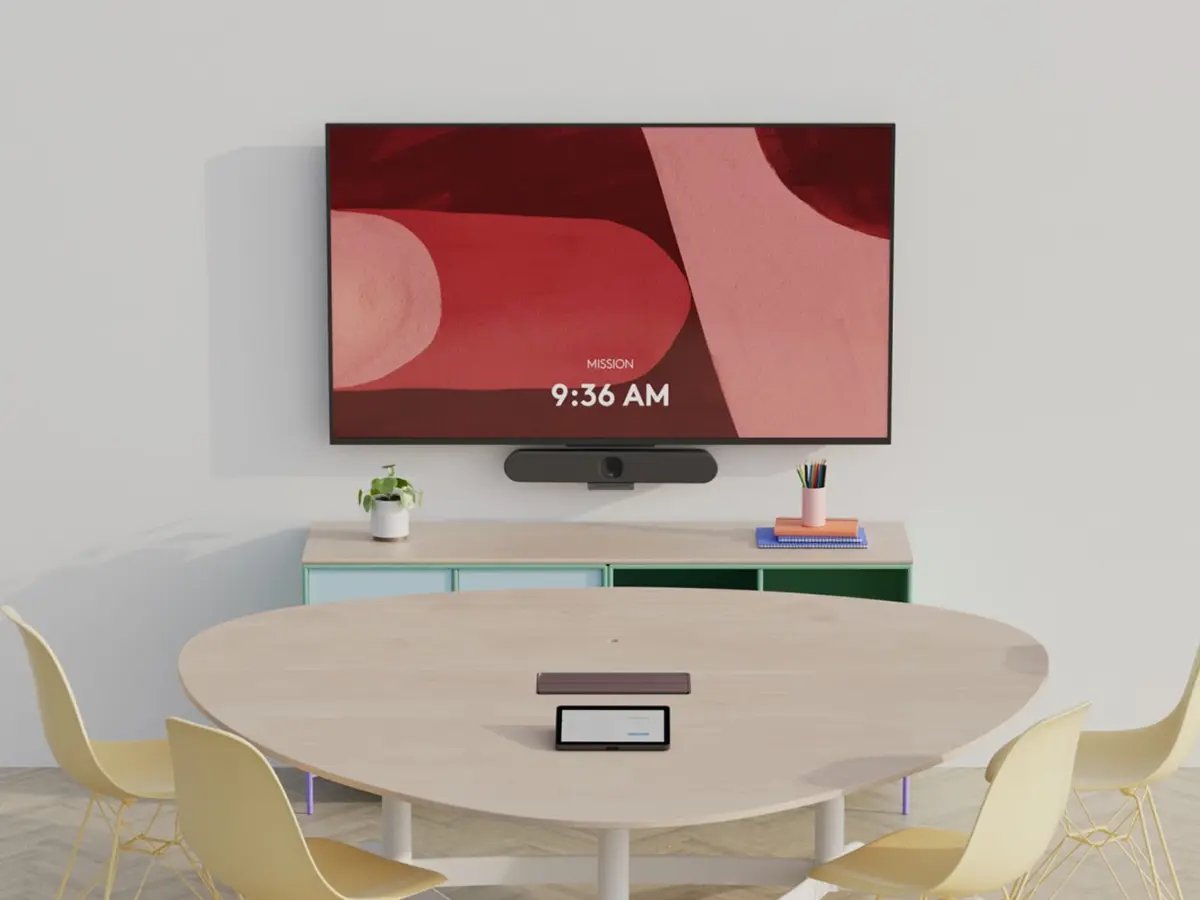 Minimalist conference room with a round table and four chairs. A large screen displays abstract art and the time, 9:36 AM. Calm and modern ambiance.