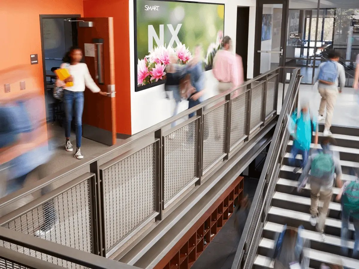 Blurred students walk through a bright school hallway. A large floral poster reads 