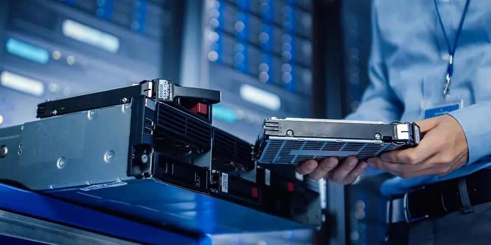 Person handling a hard drive near server equipment, representing secure data erasure and storage management.