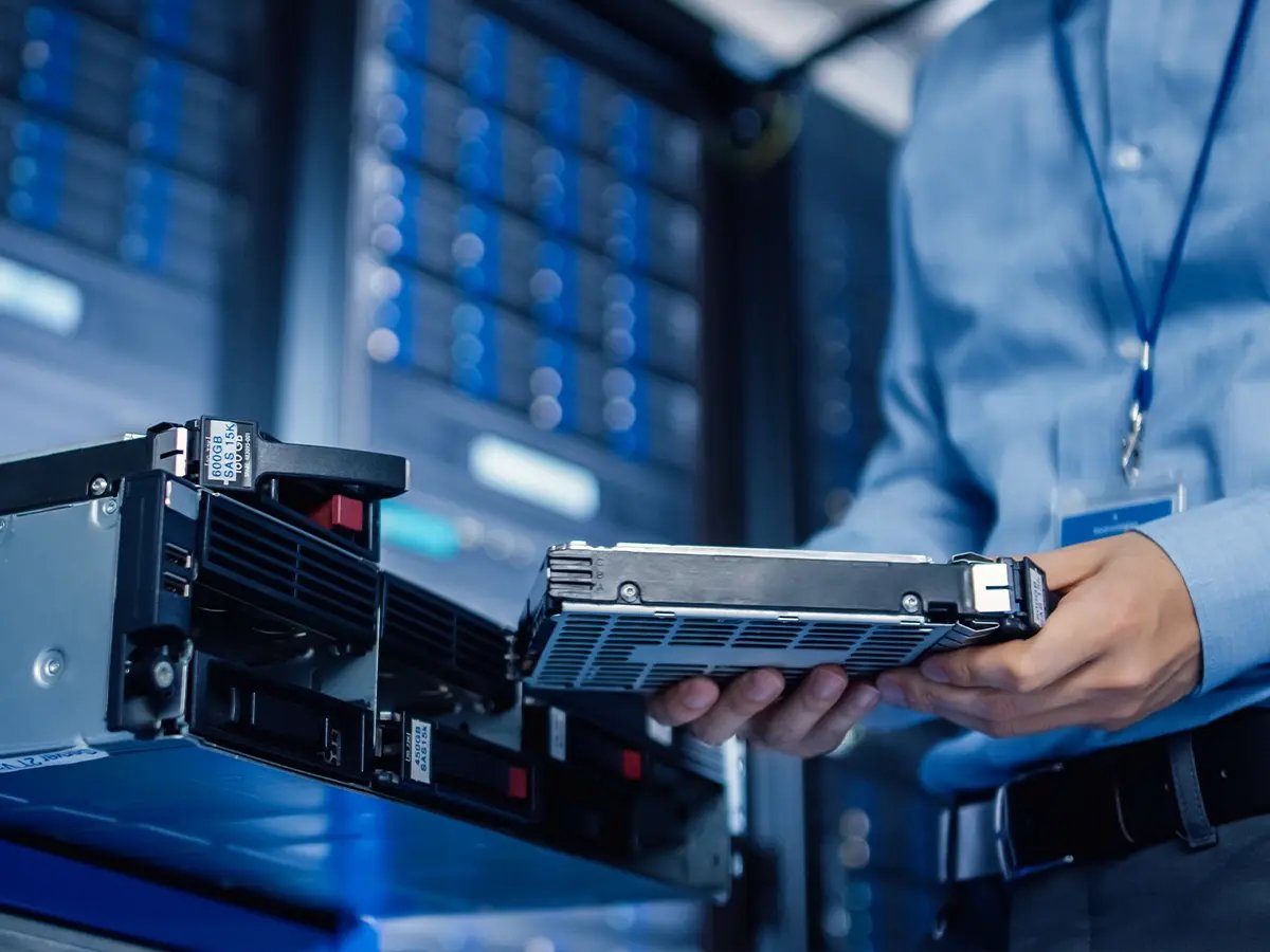 Person handling a hard drive near server equipment, representing secure data erasure and storage management.