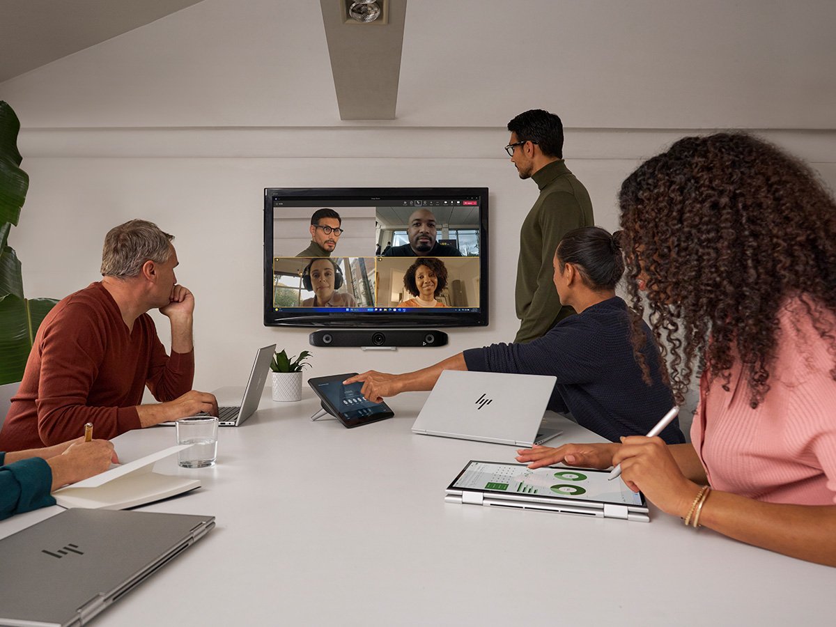 A team of 5 people with their HP notebooks in a meeting room, facing a screen on a wall, with people on a conference call
