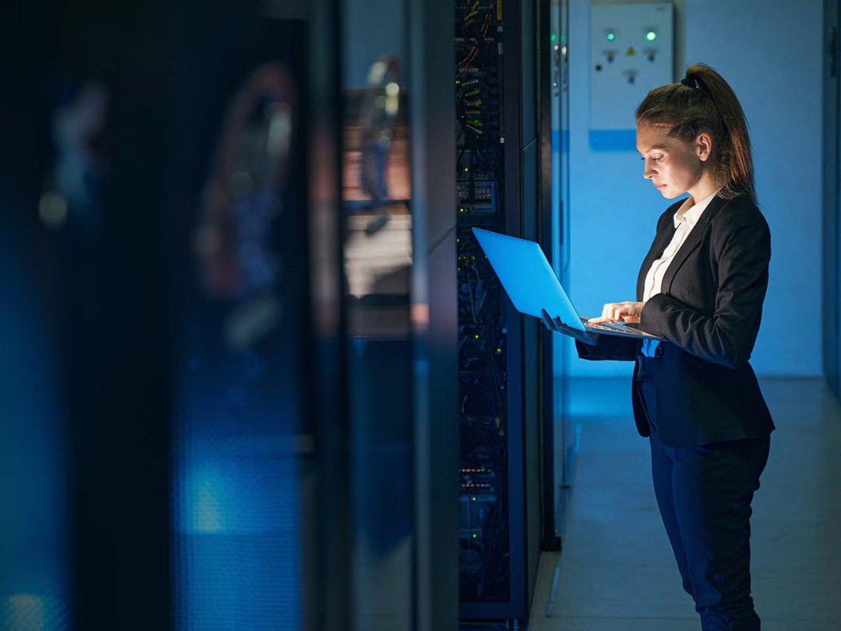 A person standing next to a server rack while working on their laptop