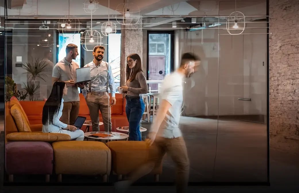 Group of coworkers chatting in a glass-walled office while a person walks past in motion blur