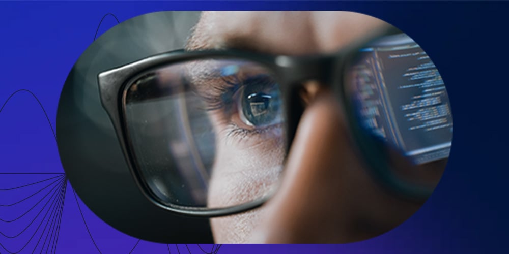 Close-up of an eye behind glasses with code reflected on the lenses
