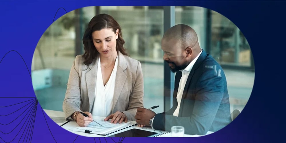 Two professionals reviewing documents together at a table in a modern office