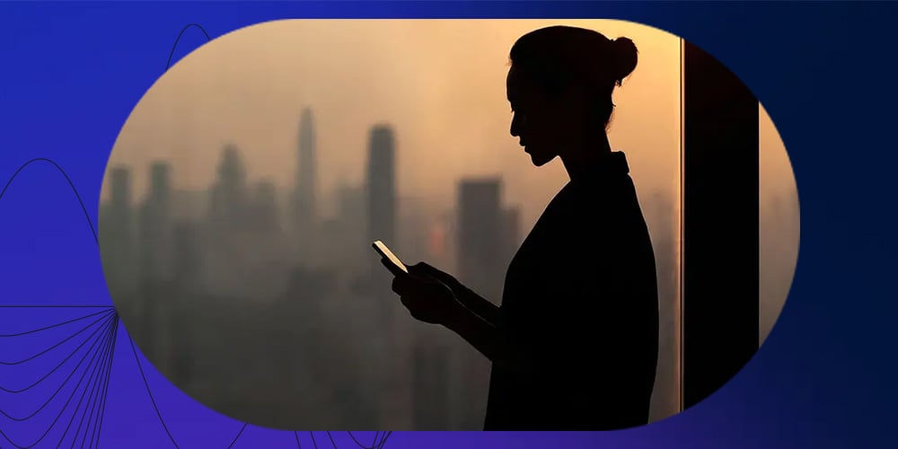 Silhouette of woman using a phone with a blurred city skyline at sunset in the background