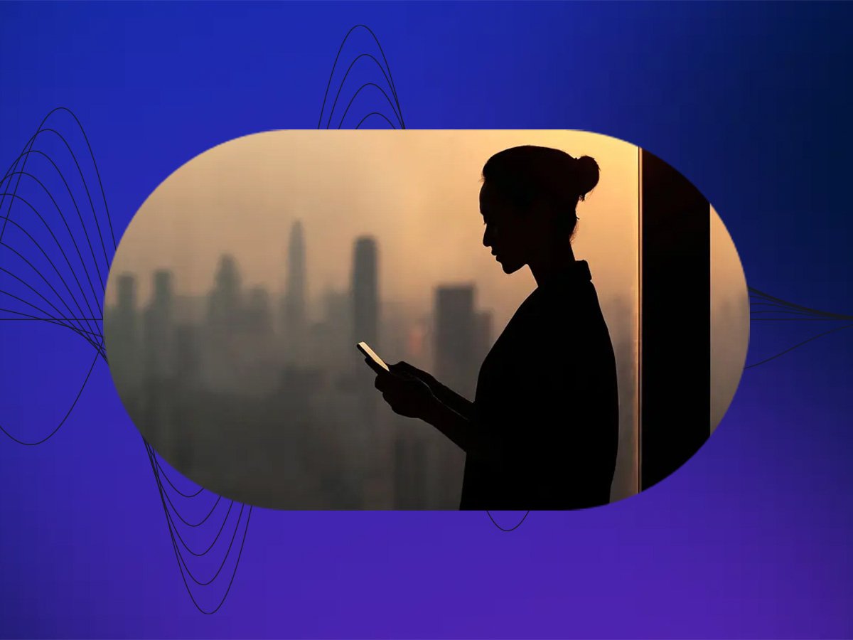 Silhouette of woman using a phone with a blurred city skyline at sunset in the background