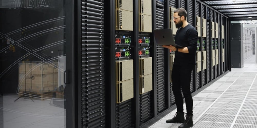 Person inspecting server racks while using a laptop in a data center.