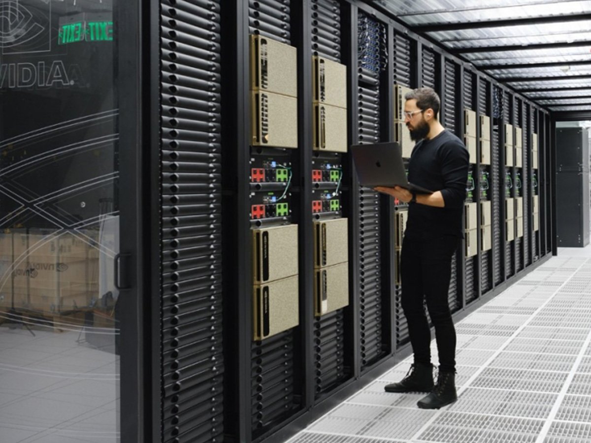 Person inspecting server racks while using a laptop in a data center.