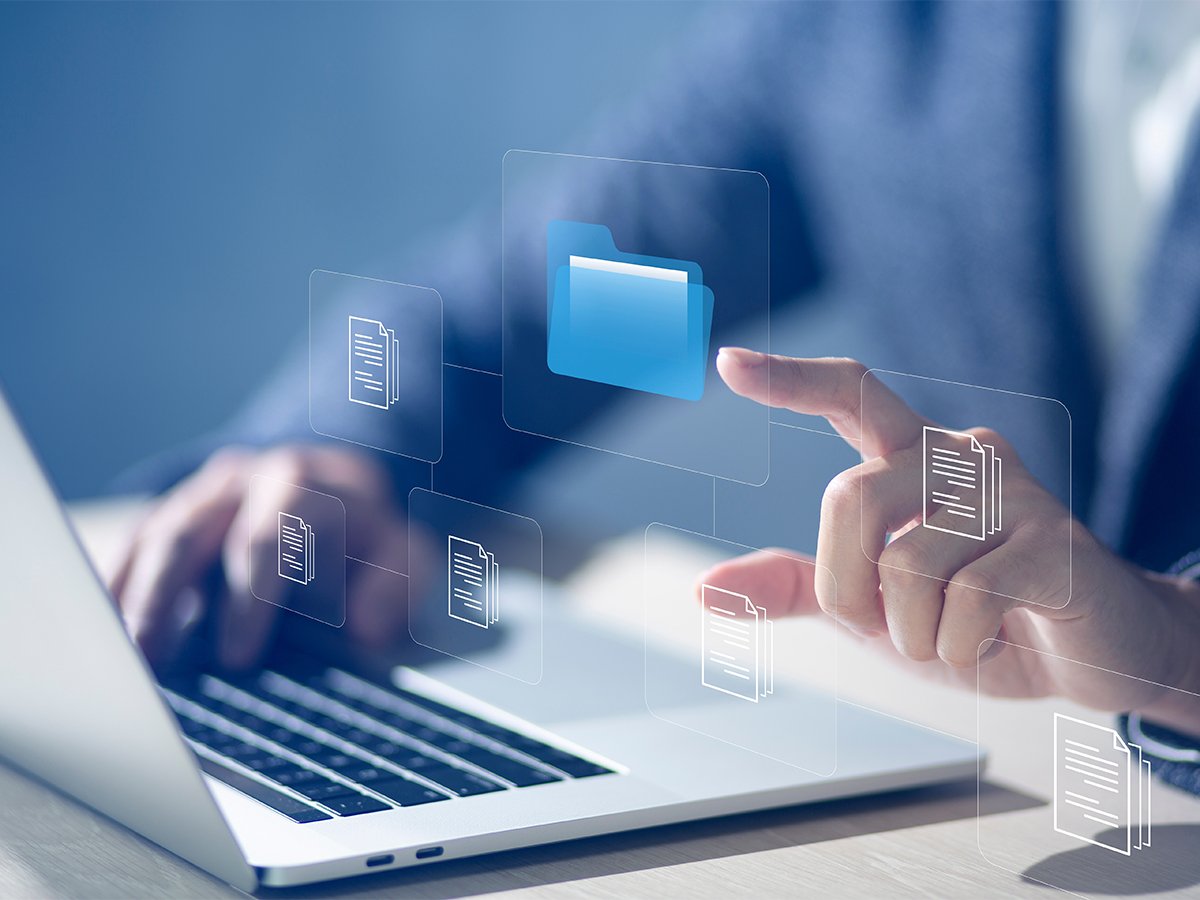 Close-up of a person using a laptop and interacting with virtual desktop folders and document icons on a transparent interface.