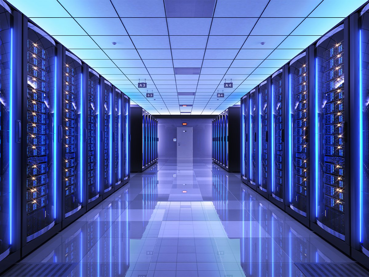Brightly lit data center hallway with rows of server racks on both sides, featuring blue LED lights and reflective flooring.
