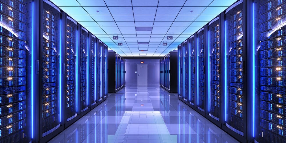 Brightly lit data center hallway with rows of server racks on both sides, featuring blue LED lights and reflective flooring.